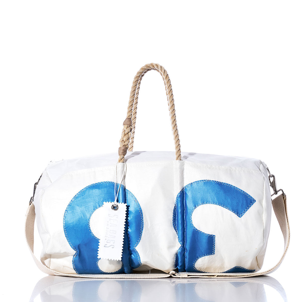 The Sea Bags Vintage 38 Duffel is a white duffel bag made from recycled sail cloth, featuring oversized blue 3 and 6 sail insignias on the front, rope handles, a beige shoulder strap, and an attached white tag for an authentic vintage duffel look. by Sea Bags