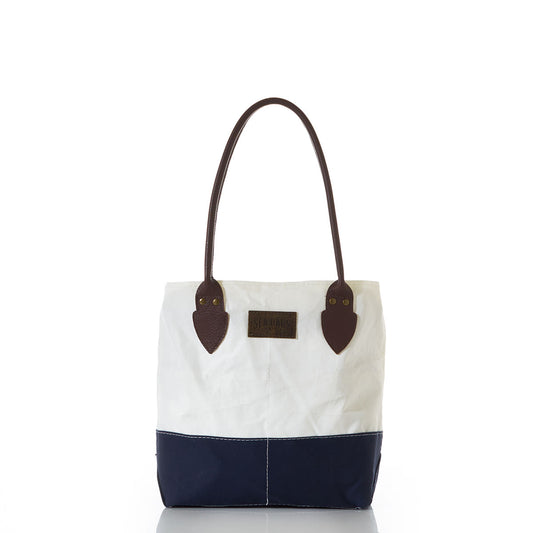 The Sea Bags Chebeague Handbag features a white and navy canvas design, brown leather handles, and a rectangular patch on the front, displayed against a plain white background. Part of the Chebeague Collection, this nautical tote evokes classic maritime style. by Sea Bags