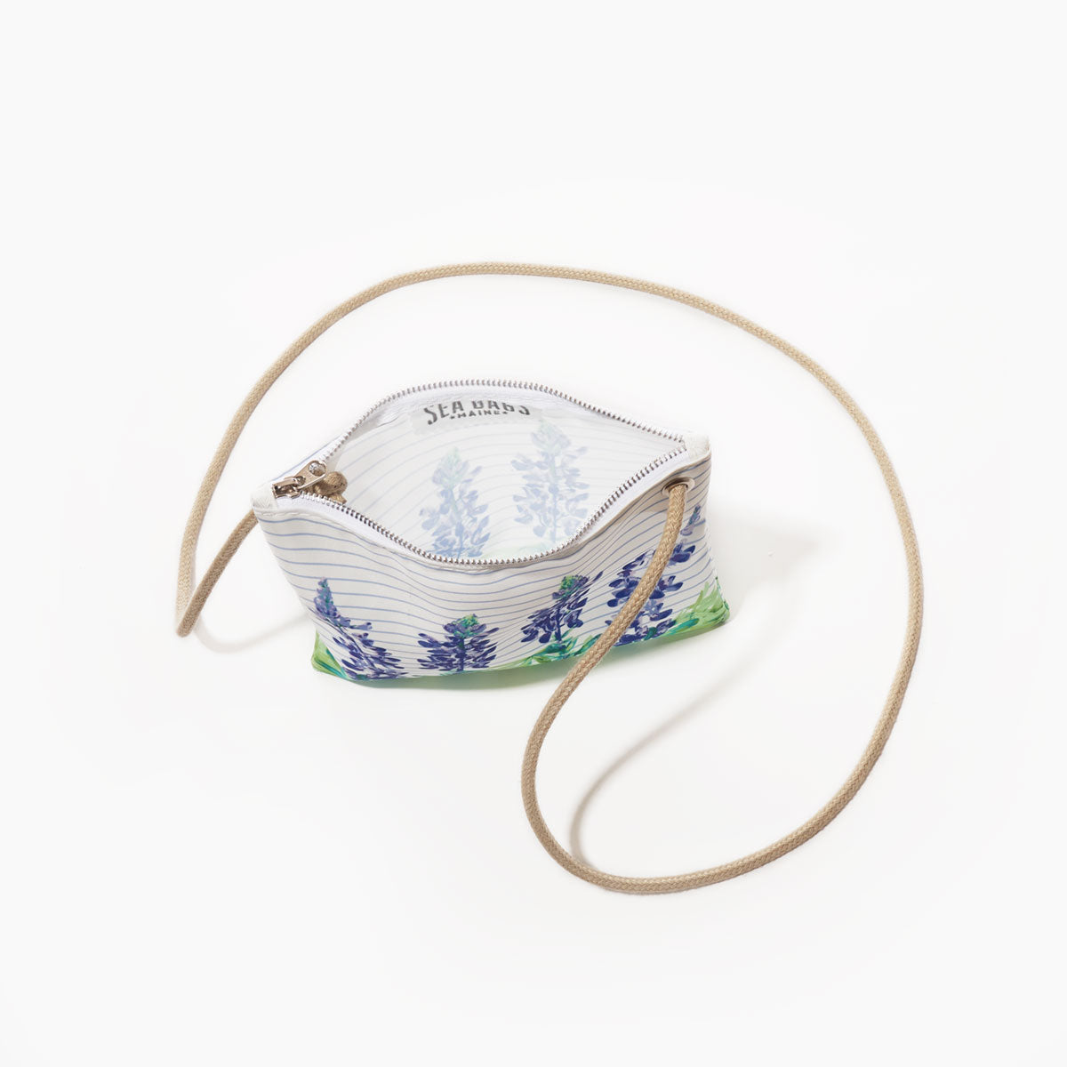 The Lupine Sailor Stripe Slim Crossbody by Sea Bags is a small zippered pouch crafted from recycled sail cloth with a blue and green lupine floral print on a white background, complemented by a beige strap. The pouch is shown open, revealing a matching patterned lining inside. by Sea Bags