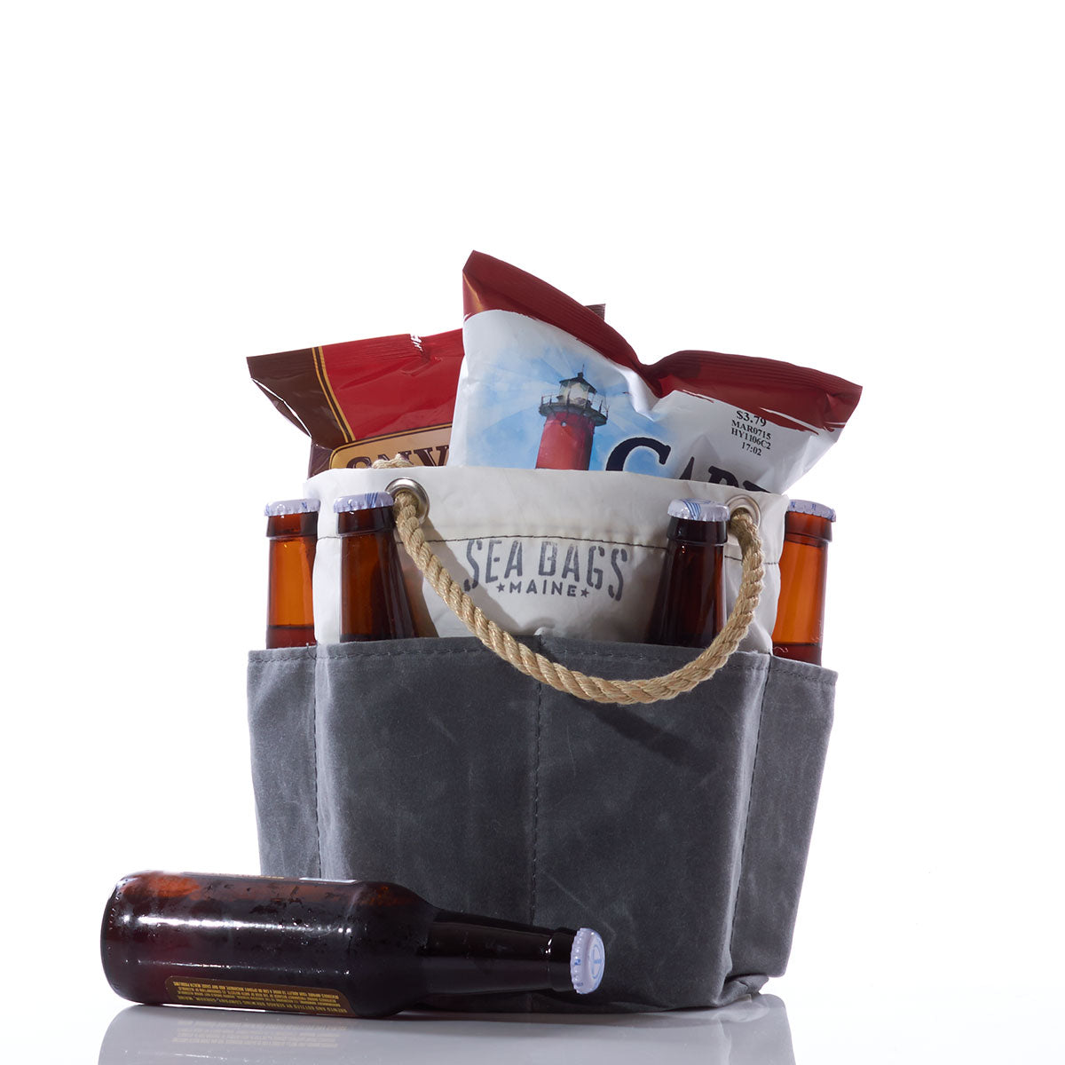 A Sea Bags All Purpose Gray Tool Bucket Bag, with sturdy rope handles and a canvas-like design, holds beer bottles and snack bags. One empty bottle rests next to the bag on a white surface. by Sea Bags