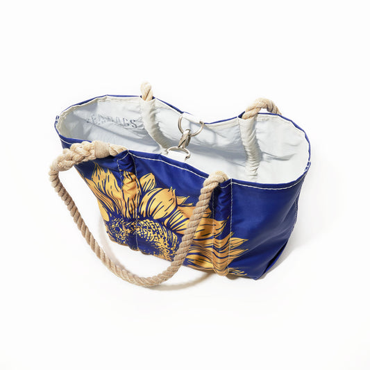 Sea Bags’ Sunflower Handbag showcases a striking sunflower print on a blue background, designed for nature enthusiasts. This everyday tote features a white interior, sturdy beige rope handles, and a secure metal clasp—perfectly blending style and function. Shown here photographed against a white backdrop. by Sea Bags