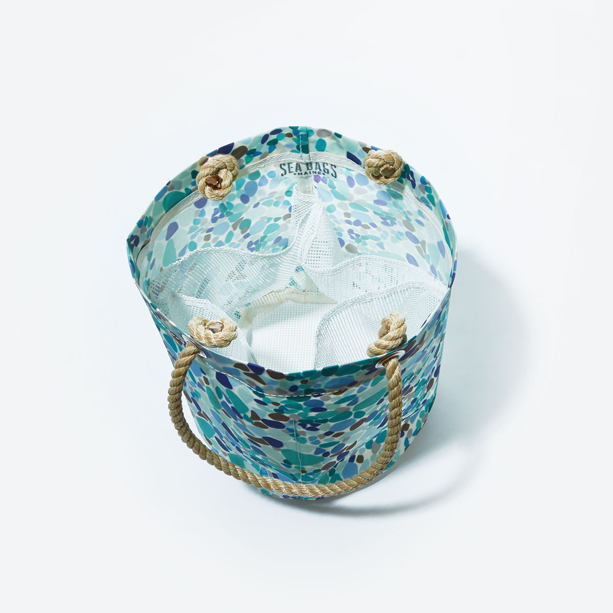 The Sea Bags Sea Glass Print Beachcomber Bucket Bag—a round tote with rope handles and a patterned design—features mesh interior compartments and is photographed from above on a white background. by Sea Bags