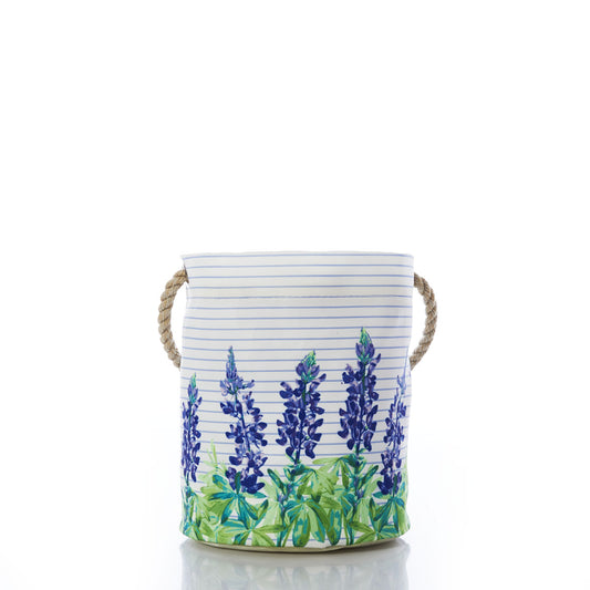 Bring coastal charm to any space with the Sea Bags Lupine Sailor Stripe Bucket—a round container featuring rope handles, horizontal blue stripes, and a delightful lupine print of bluebonnet flowers and green leaves around the base. by Sea Bags