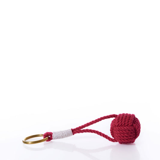 The Monkey’s Fist Keychain-Red by True showcases a classic seafaring knot in vibrant red cotton cord, expertly handcrafted with white thread detailing near the brass keyring, all displayed against a crisp white background.
