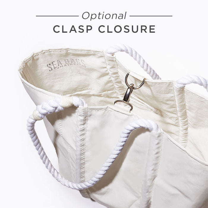 The Breton Stripe White Anchor Large Tote by Sea Bags is crafted from recycled sail cloth, featuring rope handles and an optional metal clasp closure. Shown open with the Sea Bags logo printed inside, this eco-friendly tote is both stylish and sustainable. by Sea Bags
