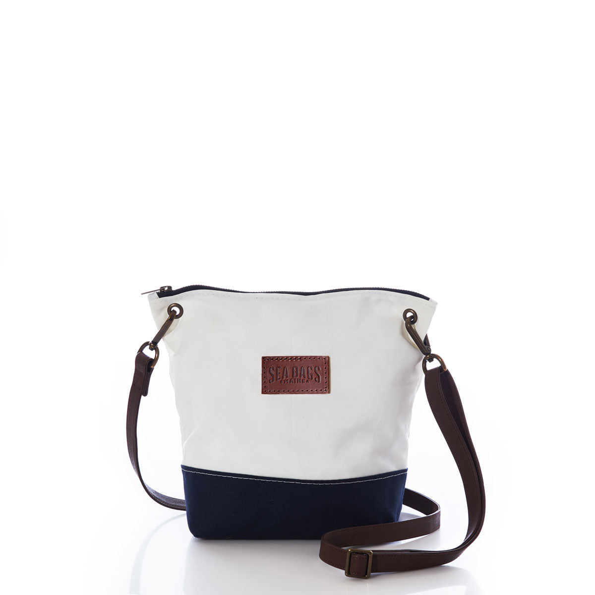 The Sea Bags Chebeague Crossbody Bag in white and navy is crafted from durable Dacron sailcloth, showcasing a brown adjustable strap, premium leather handle accents, and the signature Sea Bags patch on the front, presented against a white background. by Sea Bags