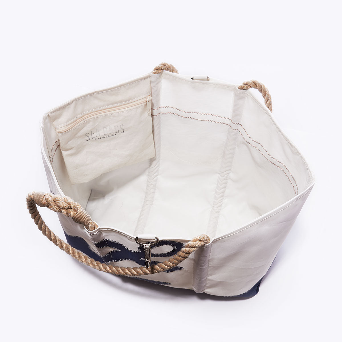 Open white canvas Navy Anchor Ogunquit Beach Tote by Sea Bags, crafted from recycled sail cloth with beige rope handles, visible interior pocket, and a bold navy anchor design on the side. Displayed on a plain light background, this stylish and eco-friendly bag is perfect for the beach. by Sea Bags