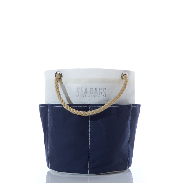 Introducing the Sea Bags All Purpose Navy Tool Bucket Bag—a small, two-tone canvas bucket bag featuring a sturdy rope handle, perfect for stylishly carrying your gardening tools. The top half is white with Sea Bags printed on it, while the bottom half is navy blue. by Sea Bags