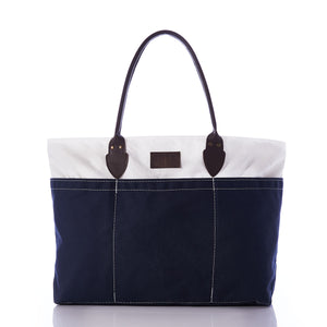 The Chebeague Large Travel Tote by Sea Bags is a spacious, water-resistant canvas bag featuring dark handles, a white upper section, and a navy blue lower section, showcased against a white background. by Sea Bags