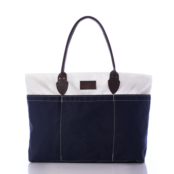 The Chebeague Large Travel Tote by Sea Bags is a spacious, water-resistant canvas bag featuring dark handles, a white upper section, and a navy blue lower section, showcased against a white background. by Sea Bags