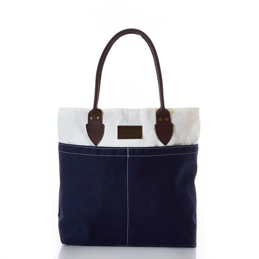 The Chebeague Tote by Sea Bags features a two-tone sailcloth design with a dark blue bottom and white top, accented by brown leather handles and visible stitching. The bag stands upright against a white background. by Sea Bags
