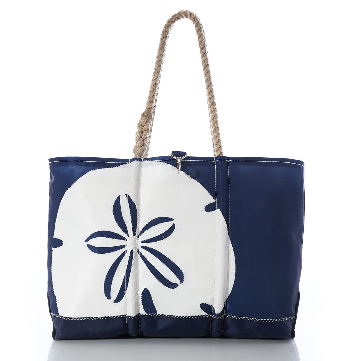 The White on Navy Sand Dollar Ogunquit Beach Tote by Sea Bags features a large white sand dollar design on the front, sturdy rope handles, and is expertly crafted from recycled sail cloth. Displayed against a white background, this eco-friendly navy blue beach bag is the ideal companion for your seaside adventures. by Sea Bags