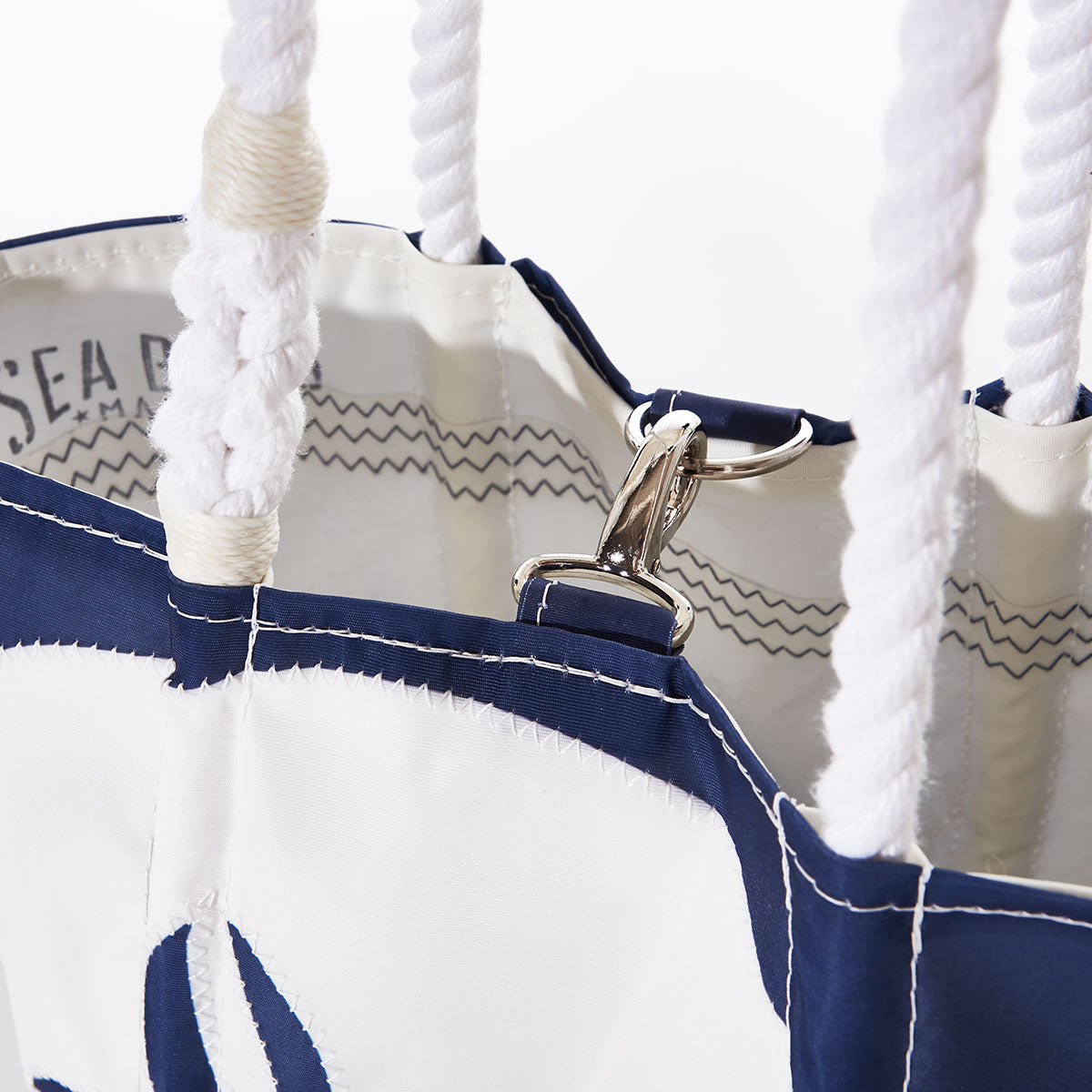 Close-up of the White on Navy Sand Dollar Handbag by Sea Bags, crafted from recycled sail cloth in blue and white, featuring thick rope handles and a metal clasp attached to an inner loop. by Sea Bags