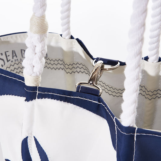 Close-up of the White on Navy Sand Dollar Handbag by Sea Bags, crafted from recycled sail cloth in blue and white, featuring thick rope handles and a metal clasp attached to an inner loop. by Sea Bags