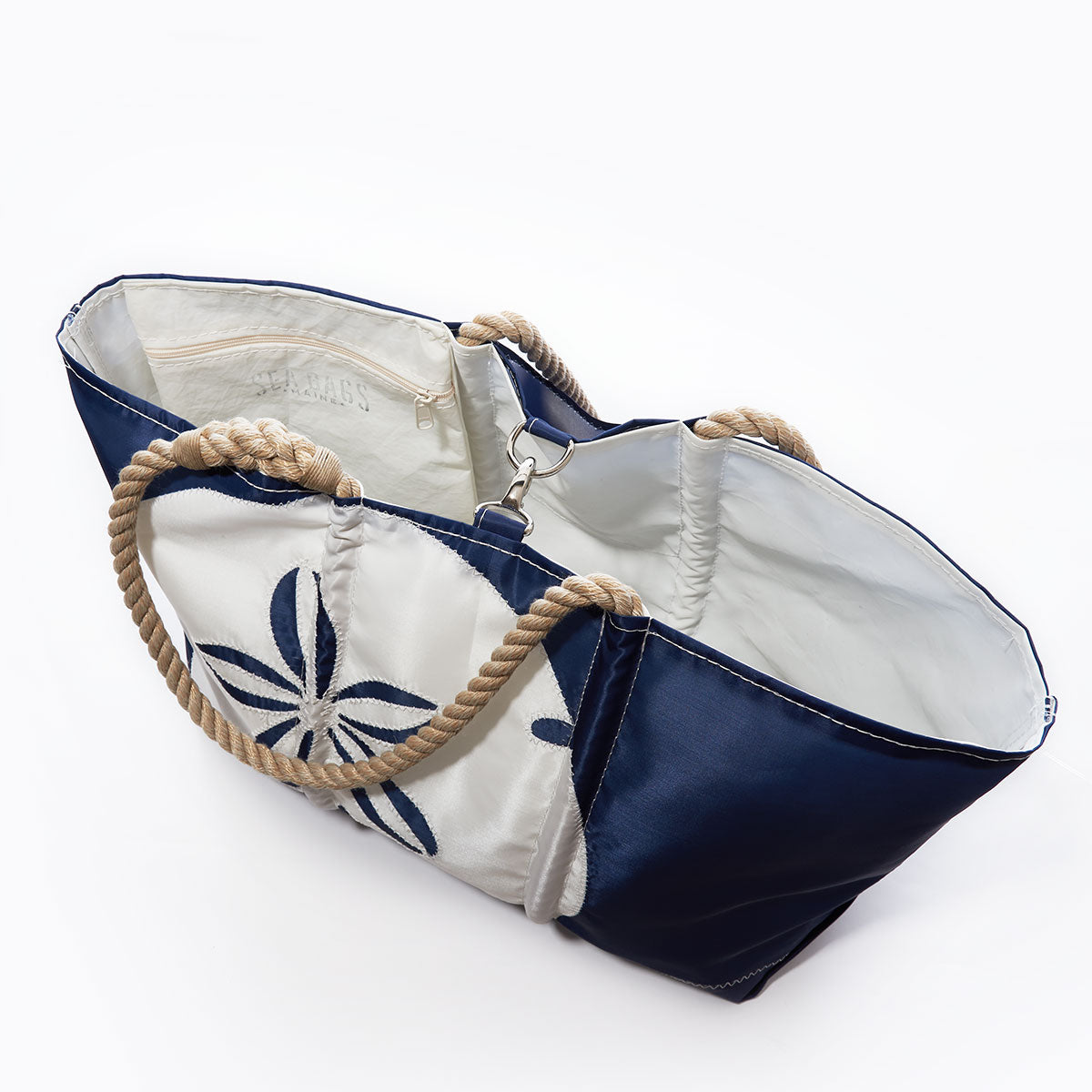 Introducing the White on Navy Sand Dollar Ogunquit Beach Tote by Sea Bags—a stylish beach tote featuring rope handles, a striking sand dollar design on navy with white accents, an open top that reveals a white interior with an inner pocket, all thoughtfully crafted from recycled sail cloth for an eco-friendly touch. by Sea Bags