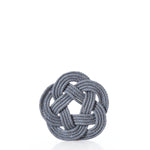 A gray rope is intricately woven into a circular Turk’s head knot, forming the Nautical Sailor Knot Coaster – Grey by Mystic Knotwork, displayed against a plain white background. by Sea Bags