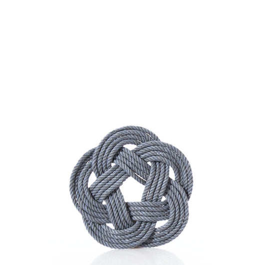 A gray rope is intricately woven into a circular Turk’s head knot, forming the Nautical Sailor Knot Coaster – Grey by Mystic Knotwork, displayed against a plain white background. by Sea Bags