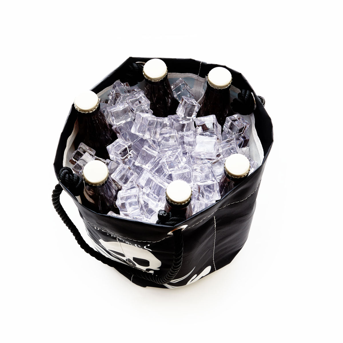 Six capped beer bottles are arranged upright in the Sea Bags Jolly Roger Beverage Bucket, a black portable drink cooler crafted from recycled sail cloth and filled with ice cubes, photographed from above on a white background. by Sea Bags