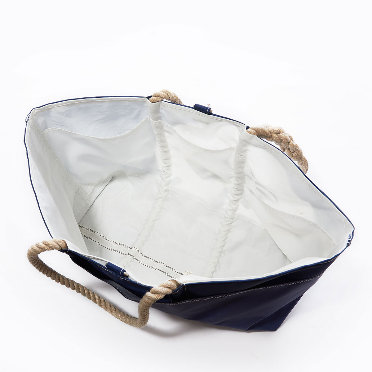 The Sea Bags White on Navy Sand Dollar Ogunquit Beach Tote, crafted from recycled sail cloth, features rope handles and a spacious white interior with simple stitching detail on the bottom—an eco-friendly tote youll love, shown here open to highlight its design. by Sea Bags