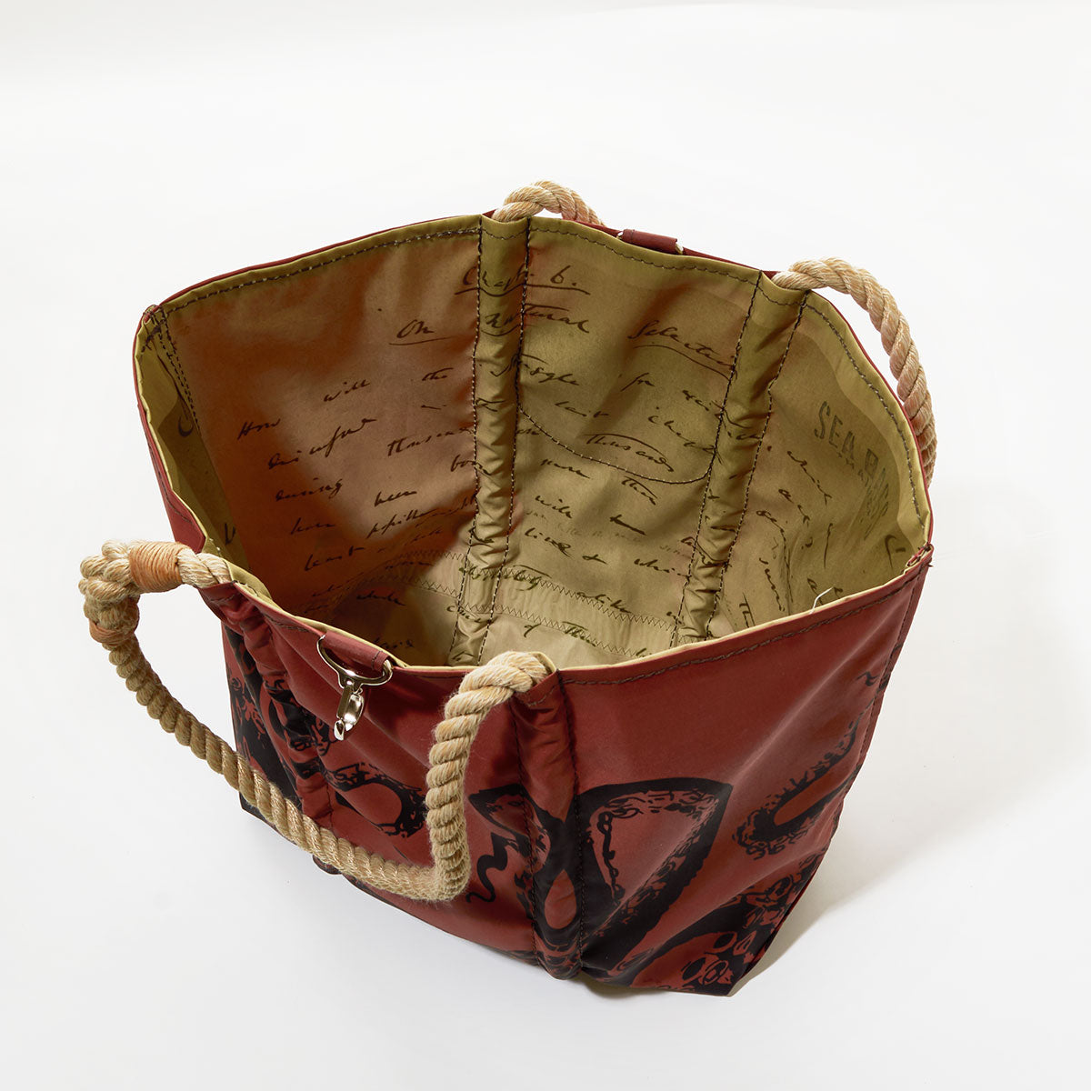 Introducing the Sea Bags Tanbark Octopus Medium Tote—a stylish open canvas bag crafted from recycled sail cloth for enhanced durability. This unique tote features sturdy rope handles, a striking red exterior adorned with a black octopus print, and an interior lining accented with cursive writing, all inspired by traditional tanbark bags. by Sea Bags