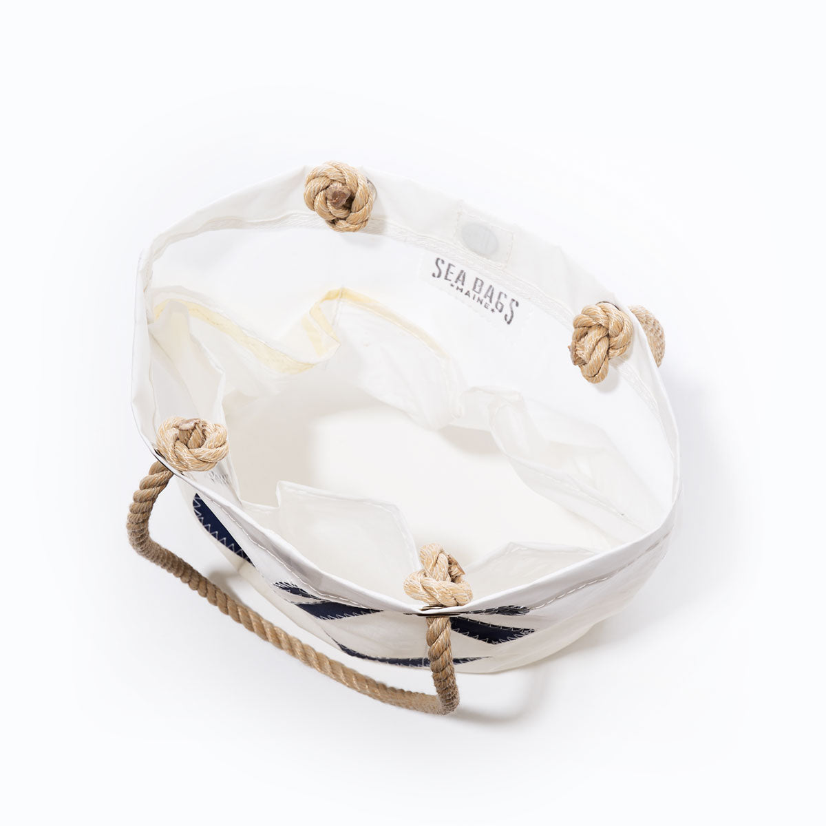 Introducing the Navy Anchor Essential Handbag by Sea Bags—a durable white canvas tote bag with rope handles and knotted corners. Designed for everyday use, this practical handbag is made from recycled sail cloth for a lightweight feel and features inner pockets with the Sea Bags name printed inside. by Sea Bags
