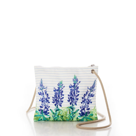 The Sea Bags Lupine Sailor Stripe Slim Crossbody showcases a blue and green lupine print on a white recycled sail cloth background, accented with a beige strap and zipper closure, and is elegantly displayed on a reflective surface. by Sea Bags