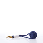 The Monkey’s Fist Keychain-Navy by true features a brass key ring attached to a navy blue knotted rope ball with a wrapped white section near the ring, creating a stylish nautical accessory set against a white background.