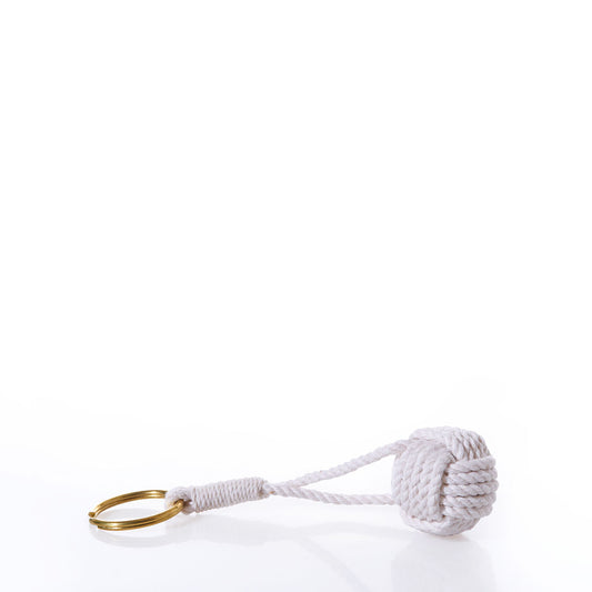 The Monkeys Fist Keychain-Natural by Mystic Knotwork features a solid brass keyring secured to a natural white cotton cord, expertly tied in the classic monkey’s fist knot. This elegant nautical keychain is photographed against a crisp white background. by Sea Bags