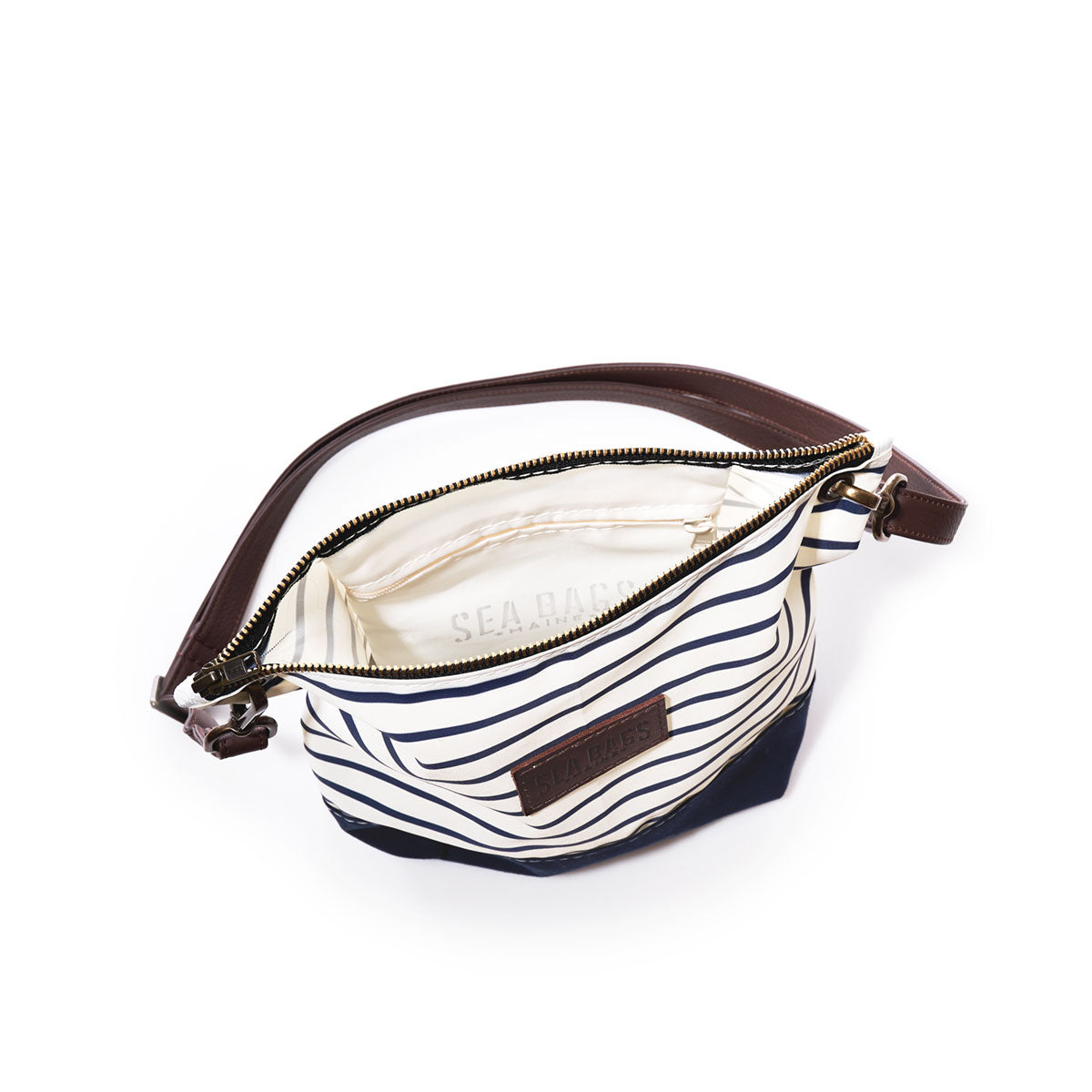 The Navy Mariner Stripe Chebeague Crossbody Bag by Sea Bags, crafted from recycled sailcloth and featuring navy and white stripes, a brown leather strap, and a branded label, is displayed open against a white background. by Sea Bags