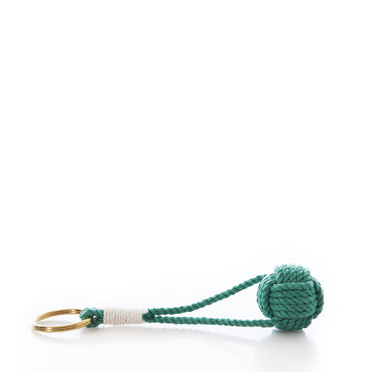 The Monkey’s Fist Keychain-Green by Mystic Knotwork features a classic green knotted rope ball attached to a brass key ring, accented with white cotton cord wrapping for a stylish nautical touch.