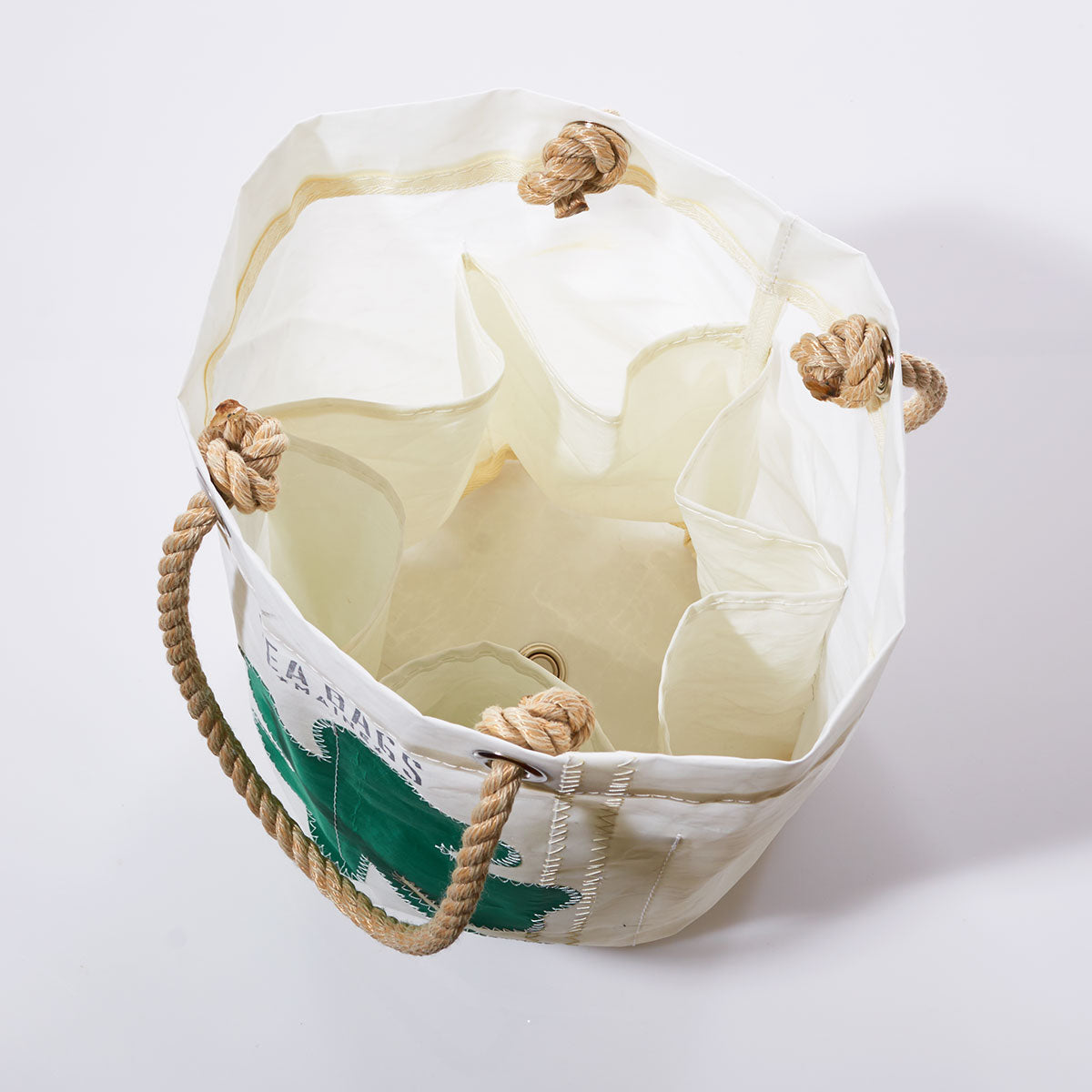 Sea Bags’ Four Leaf Clover Beverage Bucket Bag, made from recycled sail cloth, features sturdy rope handles, interior pockets, and a green four-leaf clover graphic on the exterior; shown open from above against a plain background. by Sea Bags