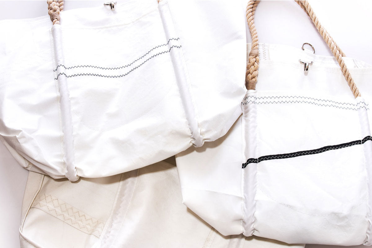 Three Sea Bags Wharf Tote bags—white with zigzag stitching and rope handles, inspired by classic sailcloth—are arranged close together on a light surface. by Sea Bags