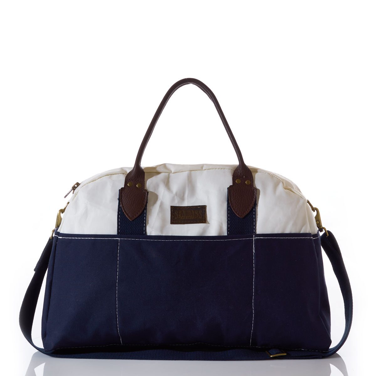 The Chebeague Weekender by Sea Bags is a two-tone weekender bag made from recycled sail cloth, featuring a white top, dark blue bottom, brown leather handles, a shoulder strap, and a small front label—all displayed against a white background. by Sea Bags