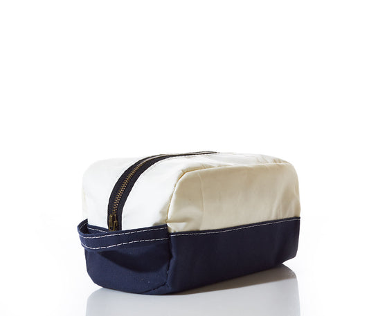 The Sea Bags Chebeague Toiletry Bag, expertly crafted from durable Dacron sailcloth, features a rectangular design with a white top, navy blue bottom, white stitching, and a zipper closure. It is shown positioned on a reflective white surface. by Sea Bags
