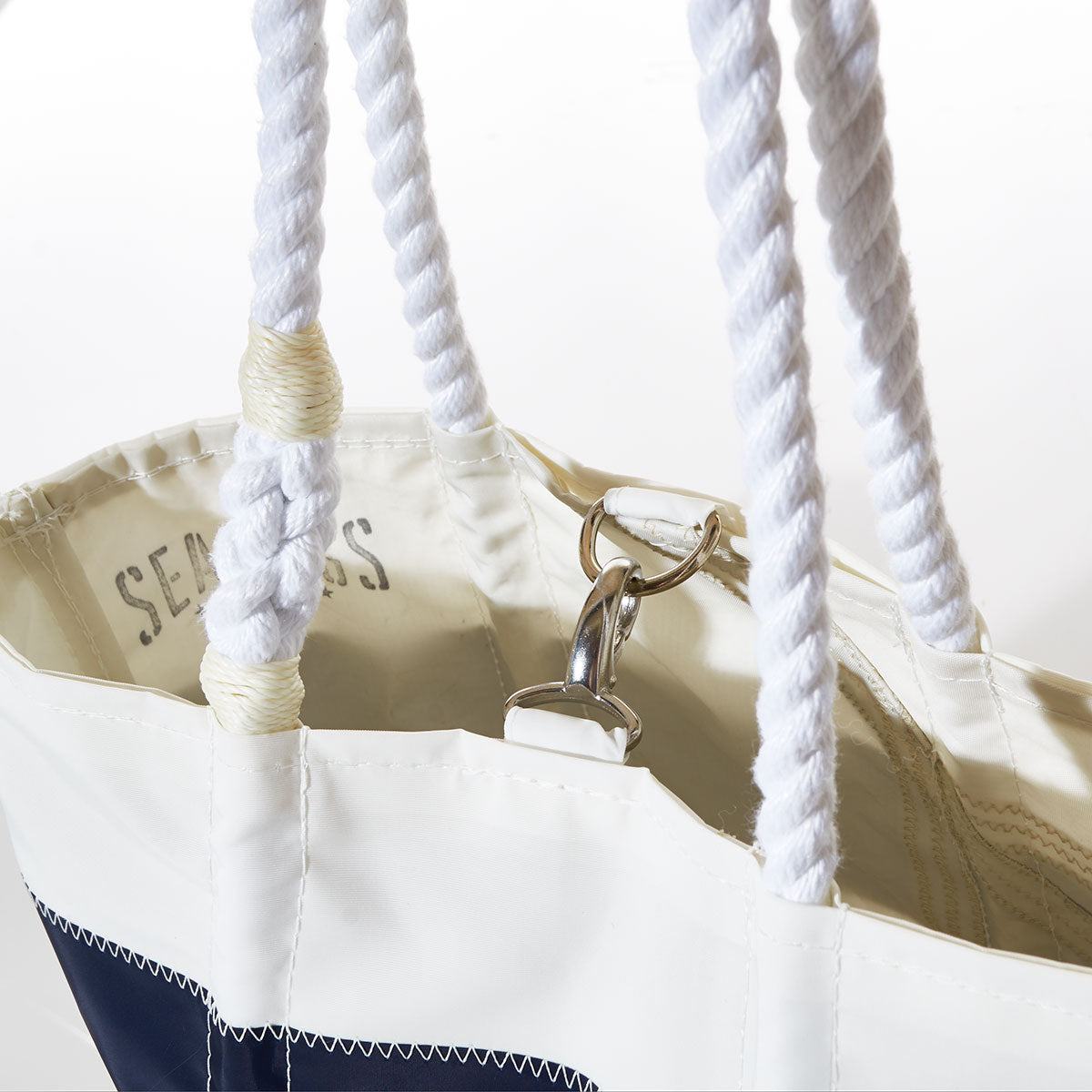 White Custom Design Handbag by Sea Bags, made from reclaimed sails, featuring thick rope handles, a visible metal clasp, and partially readable “SEABAGS” text printed on the interior. by Sea Bags