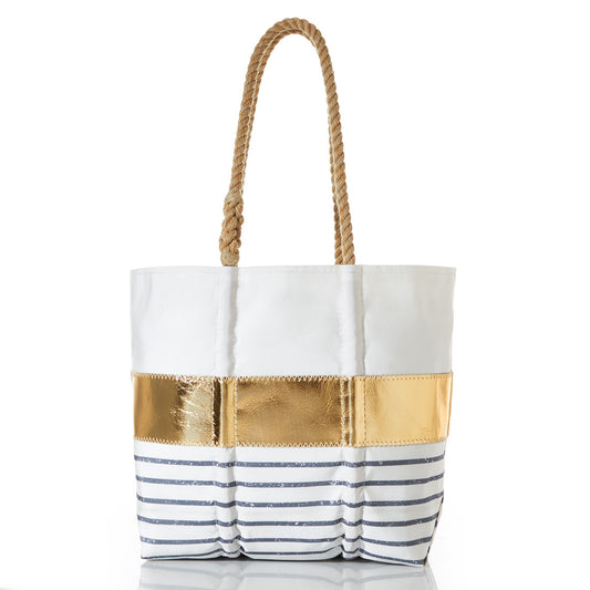 The Grey Mariner Stripe Tote by Sea Bags is a white canvas tote bag with rope handles, accented by a gold metallic horizontal stripe and classic Breton stripes in navy blue along the lower half, all set against a plain white background. by Sea Bags