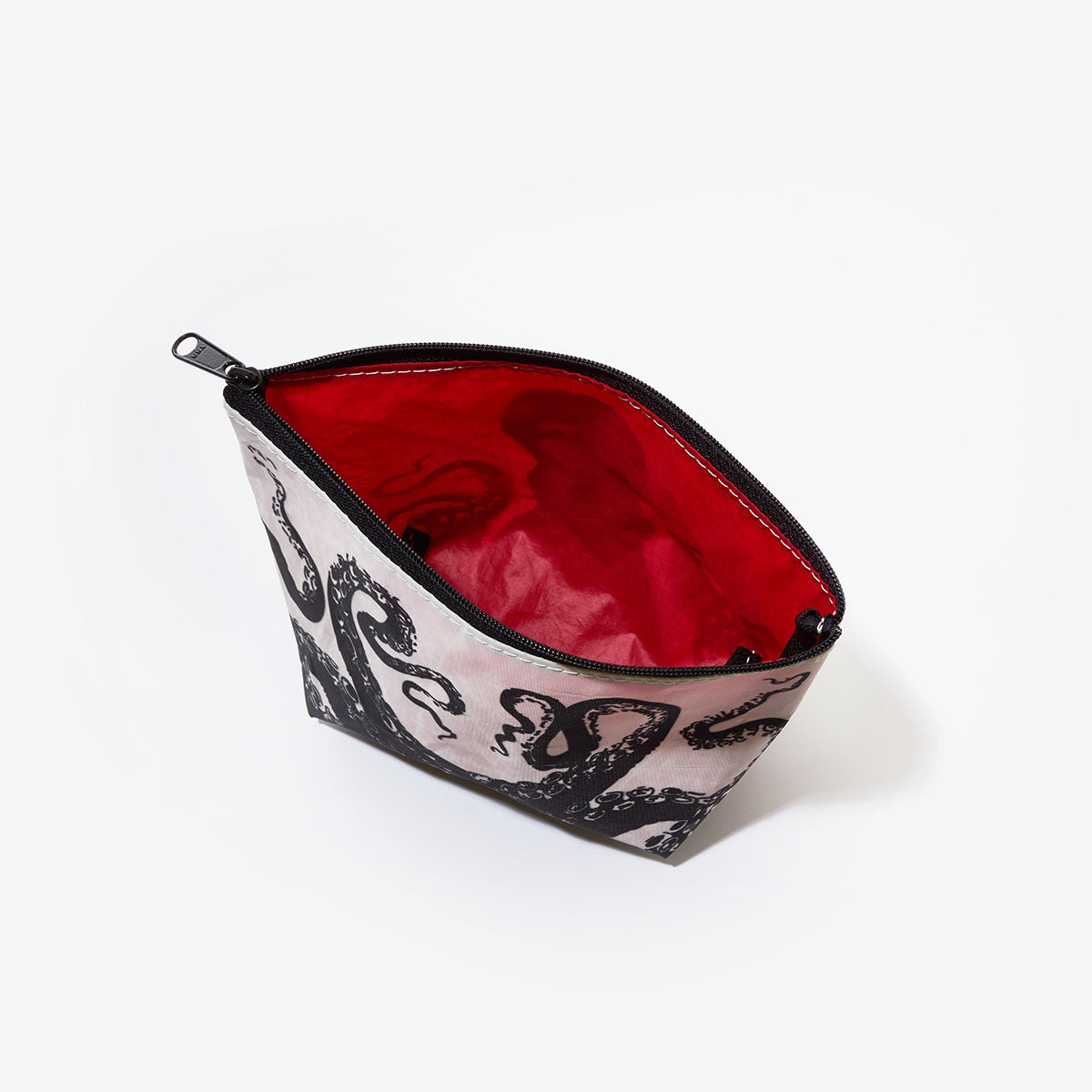 Sea Bags Octopus Cosmetic Bag, made from recycled sail cloth, showcases a striking black octopus design on the exterior and a bold red interior. Photographed from above against a white background, this zippered pouch combines eco-friendly craftsmanship with eye-catching style. by Sea Bags