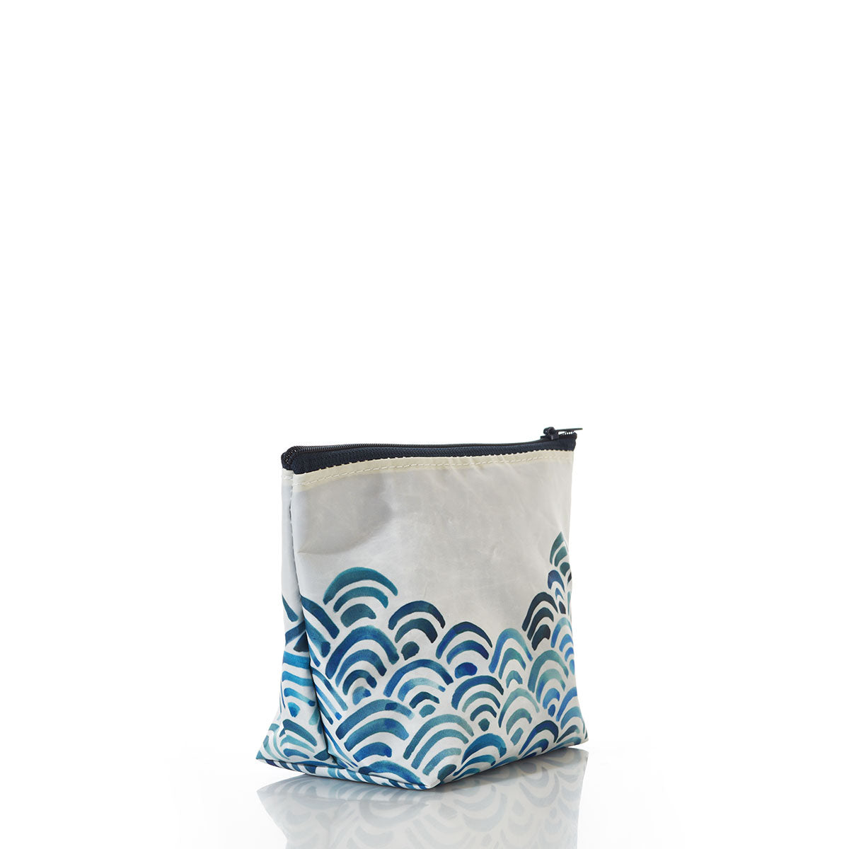The Watercolor Waves Cosmetic Bag by Sea Bags features a blue wave pattern and is crafted from recycled sailcloth; this eco-friendly accessory stands upright on a white reflective surface, offering both style and functionality for travel. by Sea Bags