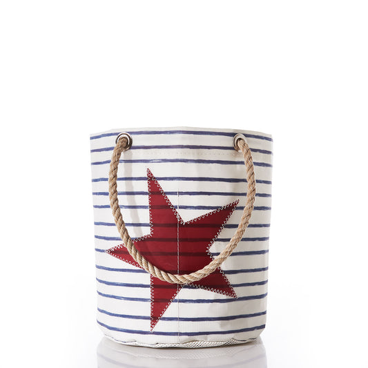 Sea Bags’ Breton Stripe and Star Beachcomber Bucket—an eco-friendly canvas tote featuring classic white and blue stripes with a bold red star design and sturdy rope handles—shown on a white background, makes the perfect companion for seaside adventures. by Sea Bags