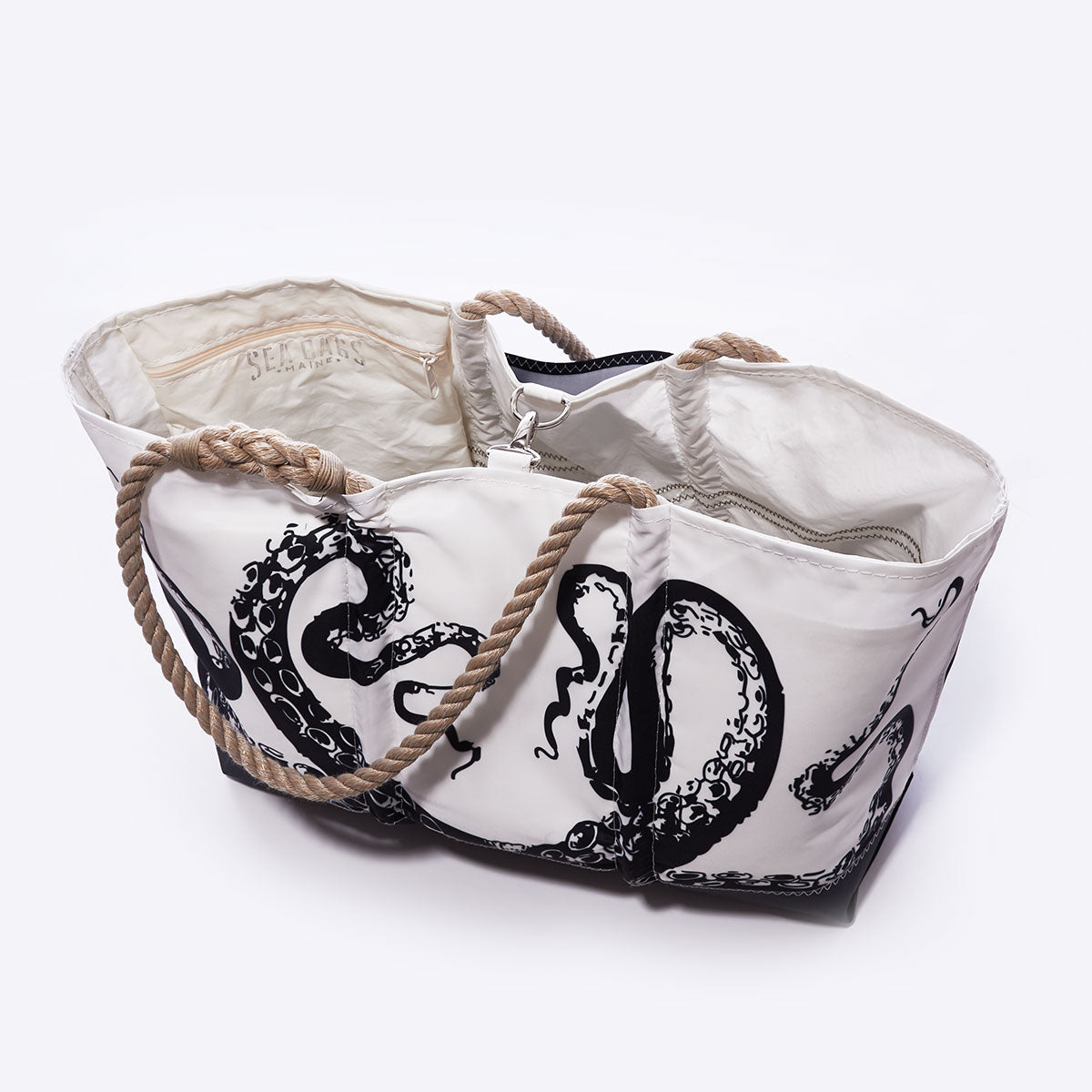 Introducing the Octopus Ogunquit Beach Tote by Sea Bags—a white bag adorned with a striking black octopus tentacle design, expertly crafted from recycled sail cloth. This tote features durable rope handles, an open top for easy access, and thoughtfully designed interior pockets and compartments, blending functional beach style with vintage-inspired illustration charm. by Sea Bags