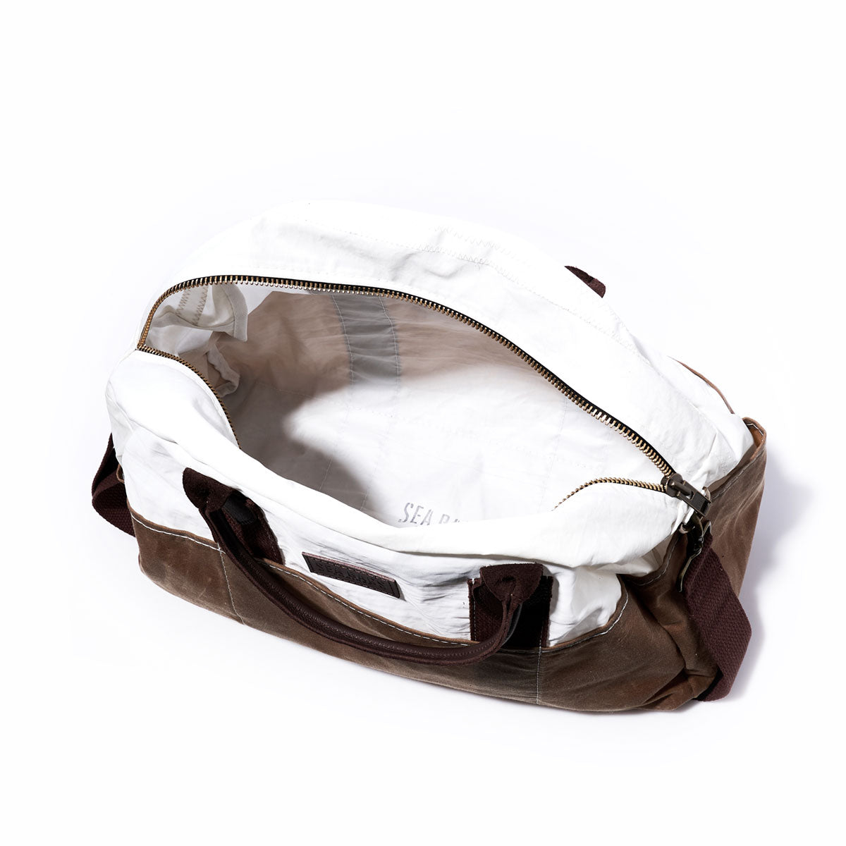 The Tan Chebeague Weekender by Sea Bags is a white and tan duffel bag crafted from recycled sail cloth, featuring an open zipper that reveals its empty interior and dark brown handles—making it the perfect unique carry-on. by Sea Bags