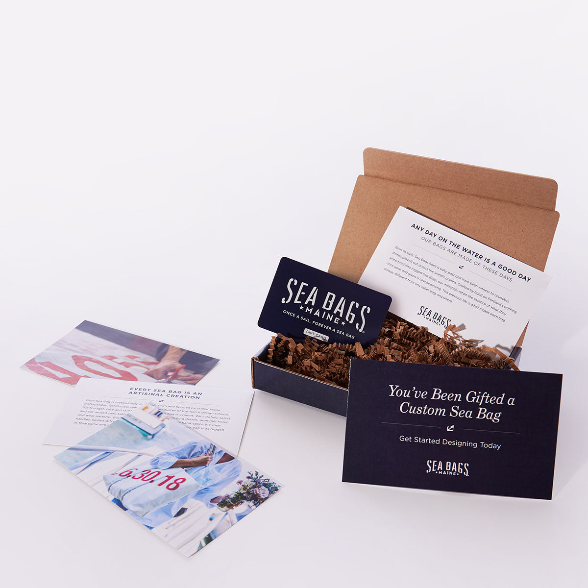 A Custom Sea Bags Gift Card from Sea Bags, presented in a stylish gift box with informational cards and shredded packing material, beautifully displayed on a white surface—an ideal Maine-inspired gift for any occasion. by Sea Bags