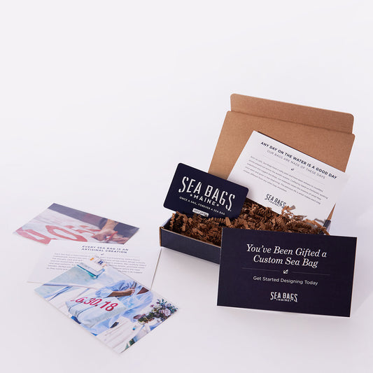 A Custom Sea Bags Gift Card from Sea Bags, presented in a stylish gift box with informational cards and shredded packing material, beautifully displayed on a white surface—an ideal Maine-inspired gift for any occasion. by Sea Bags