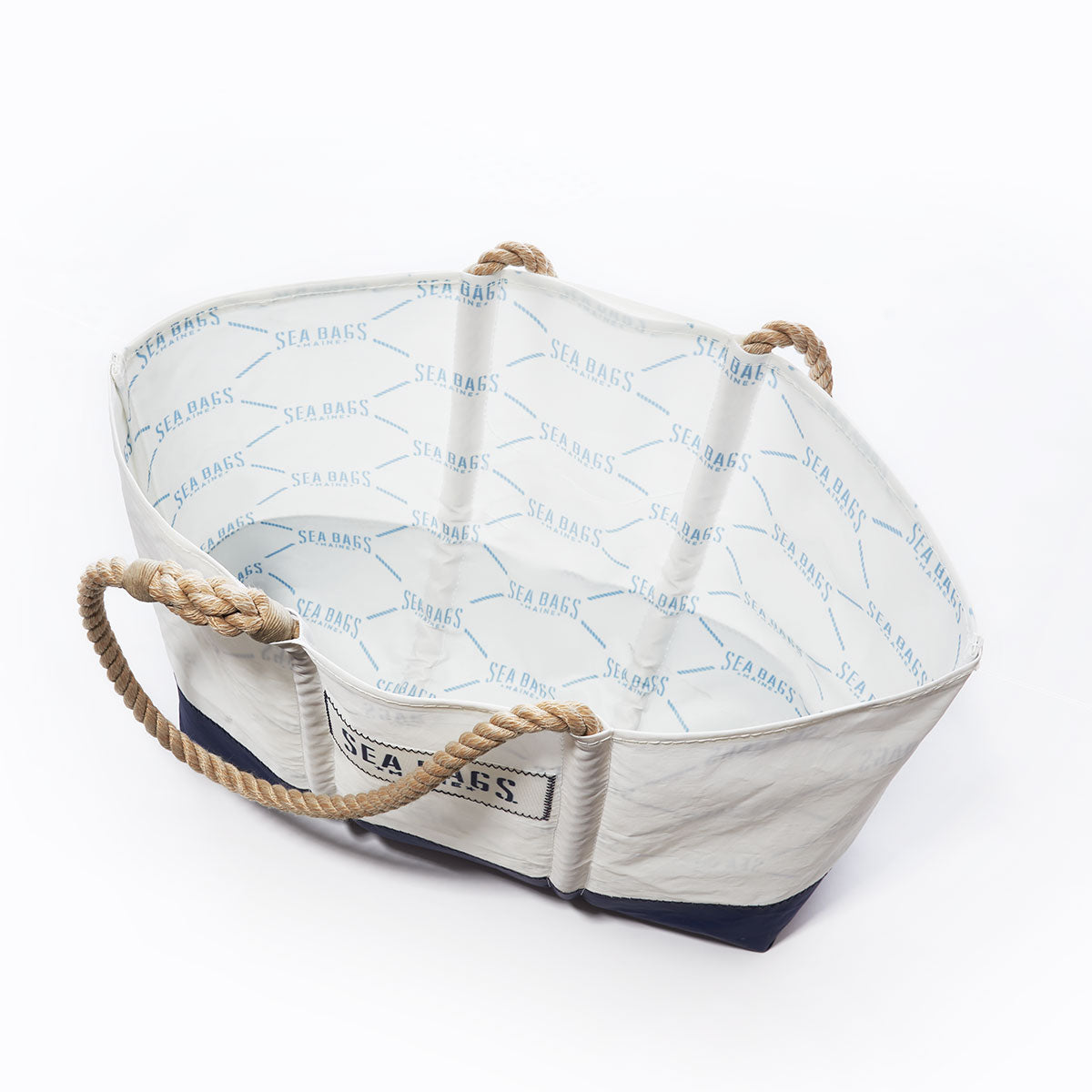 The Sailmakers Tote with Clasp and Hanging Pocket by Sea Bags is a white tote bag with rope handles, crafted from recycled sail cloth. Featuring a dark navy base, the open bag reveals Sea Bags printed on the inner lining. by Sea Bags