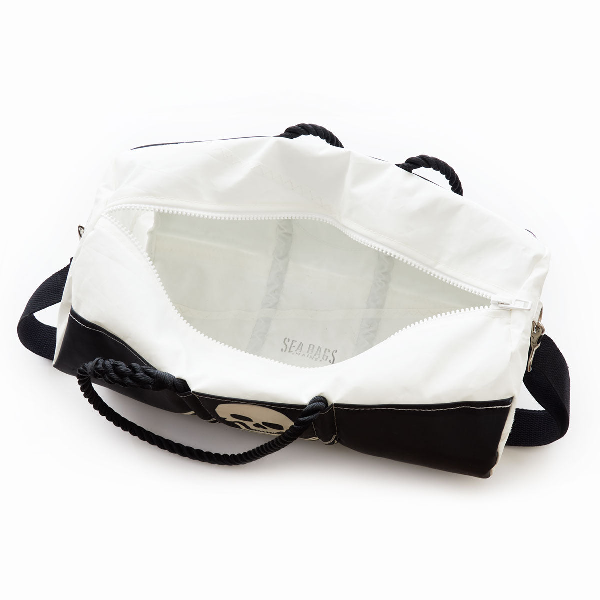 The Sea Bags Jolly Roger Duffel is a durable white and black duffel bag crafted from recycled sail, featuring a bold skull graphic and a sturdy rope handle. The partially unzipped design reveals its spacious white interior. by Sea Bags