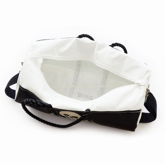 The Sea Bags Jolly Roger Duffel is a durable white and black duffel bag crafted from recycled sail, featuring a bold skull graphic and a sturdy rope handle. The partially unzipped design reveals its spacious white interior. by Sea Bags