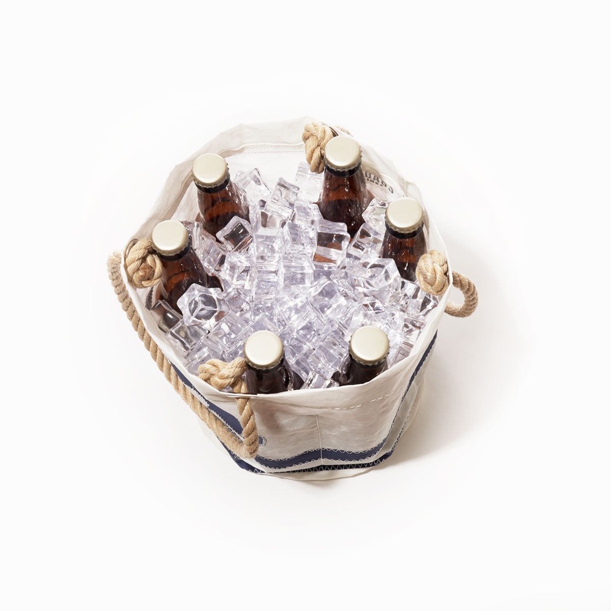 Six amber glass bottles of beer, chilled in ice, are arranged inside the Sea Bags Breton Stripe Whale Beverage Bucket—a white recycled sail cloth cooler with thick rope handles—viewed from directly above against a white background. by Sea Bags