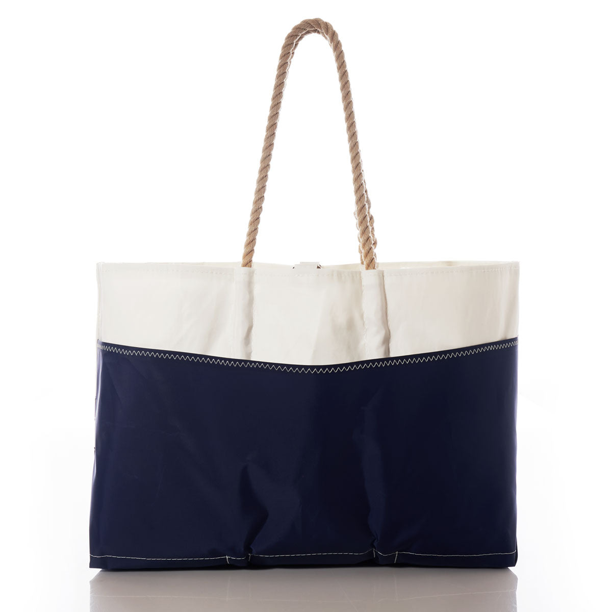 The Sea Bags Breton Stripe Whale Ogunquit Beach Tote features a navy blue bottom, white top, and thick rope handles, crafted from eco-friendly recycled sail cloth and displayed on a reflective white surface. by Sea Bags