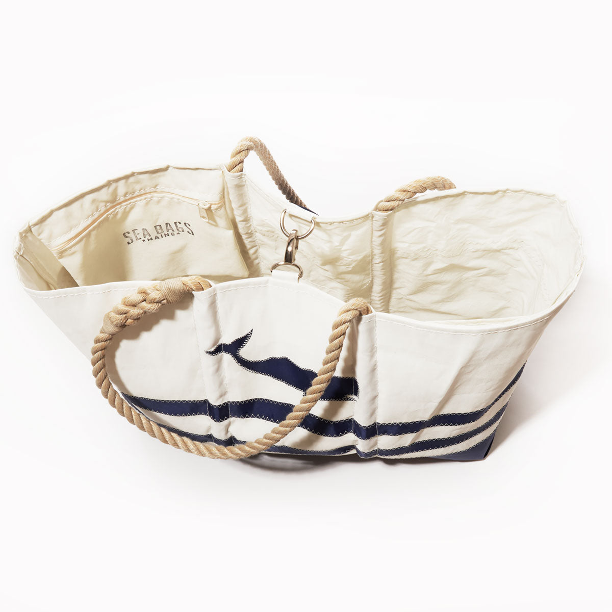 Navy whale graphic adorns the Breton Stripe Whale Ogunquit Beach Tote by Sea Bags, crafted from recycled sail cloth for eco-friendly style; this spacious white tote features rope handles and an interior pocket—perfect for nautical beach outings. by Sea Bags