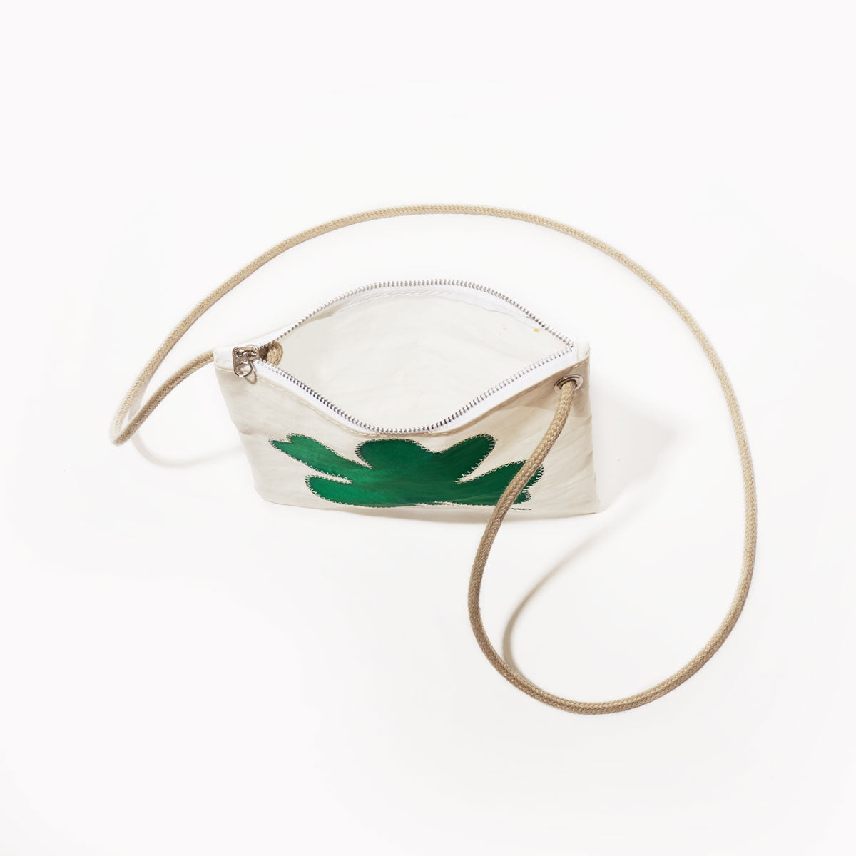 The Sea Bags Four Leaf Clover Slim Crossbody, crafted from durable sail cloth, features a green abstract clover design on the front, a beige shoulder strap, and a compact white zippered silhouette—an ideal handbag alternative—shown on a white background. by Sea Bags